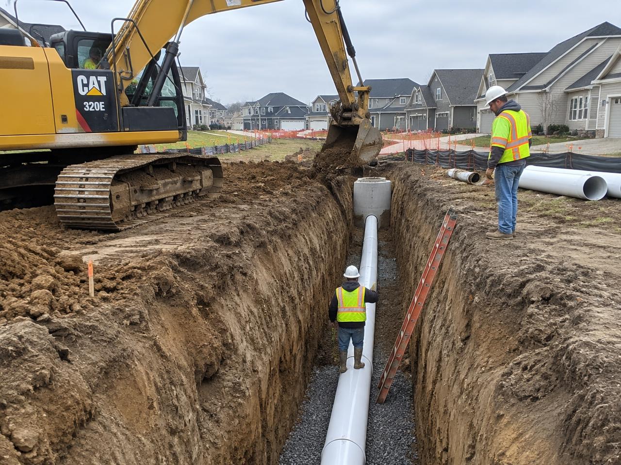 Excavator and crew installing a sewer line in a neighborhood